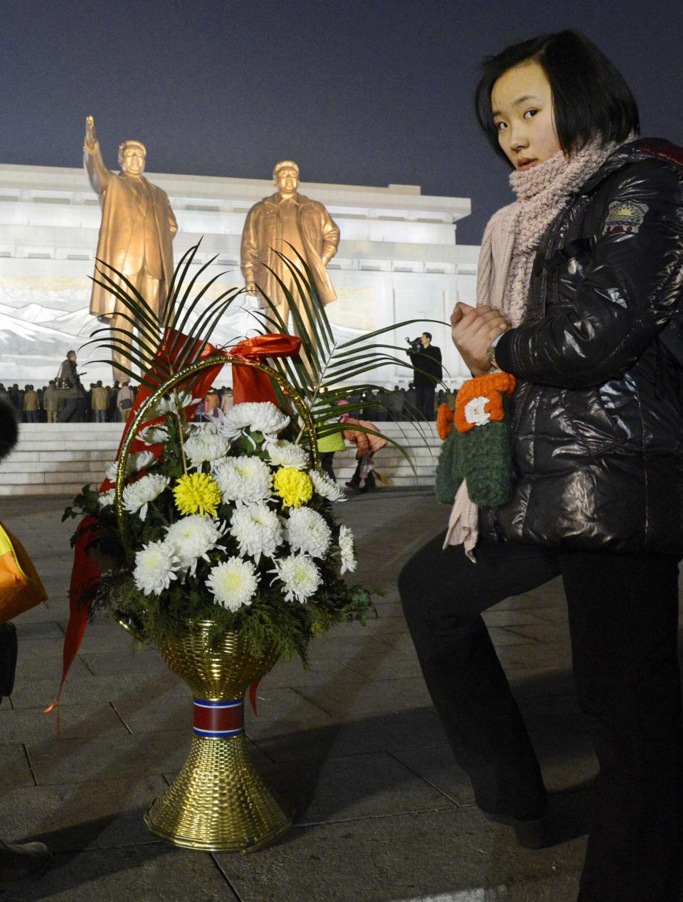 A woman stands next to flowers near bronze statues of North Korea's late founder Kim Il Sung and late leader Kim Jong Il at Mansudae in Pyongyang