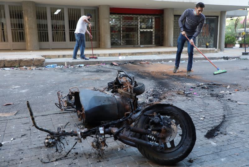 A burnt motorbike is pictured as people clean up a street in Beirut