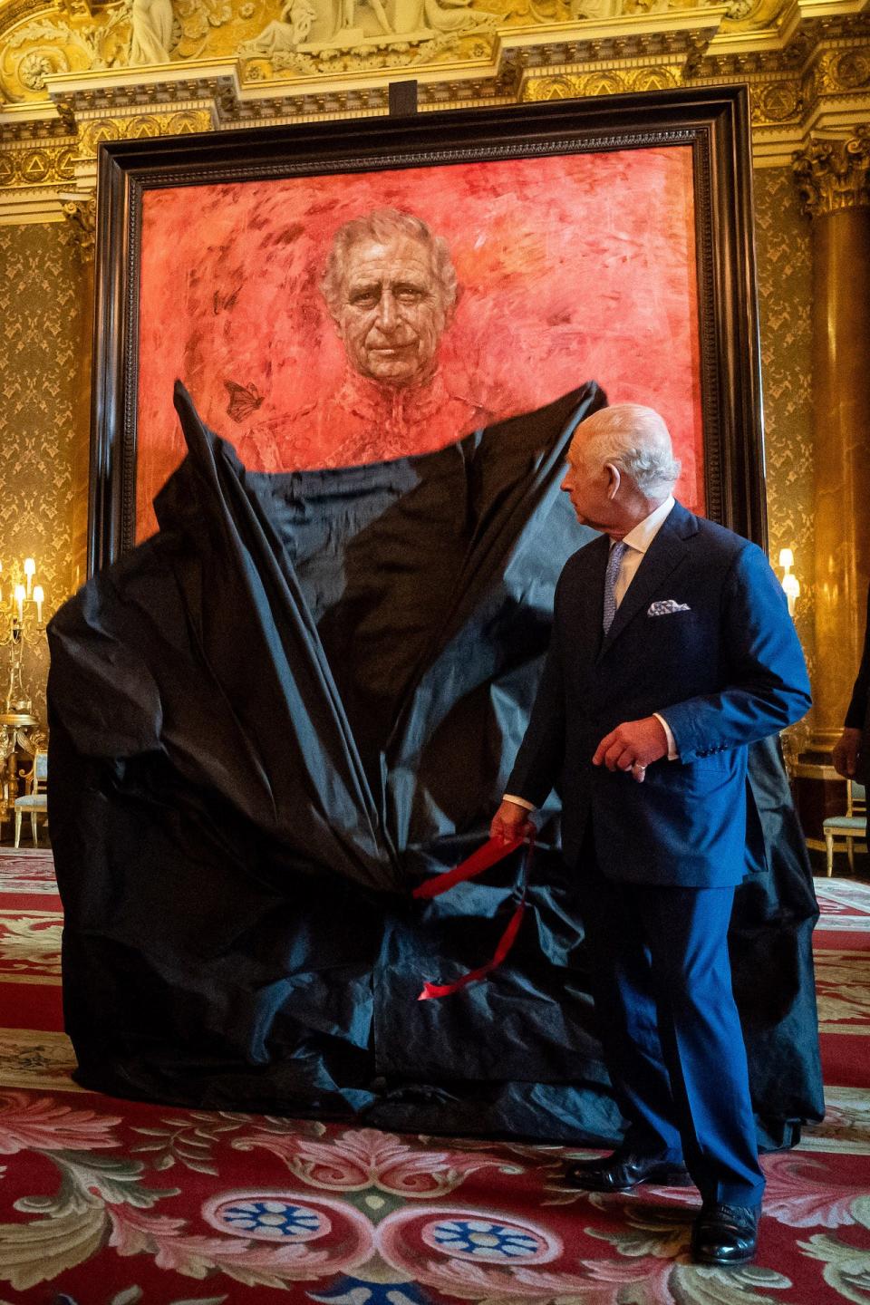 King Charles III at Buckingham Palace pulling down a black sheet to reveal his first portrait since his coronation.