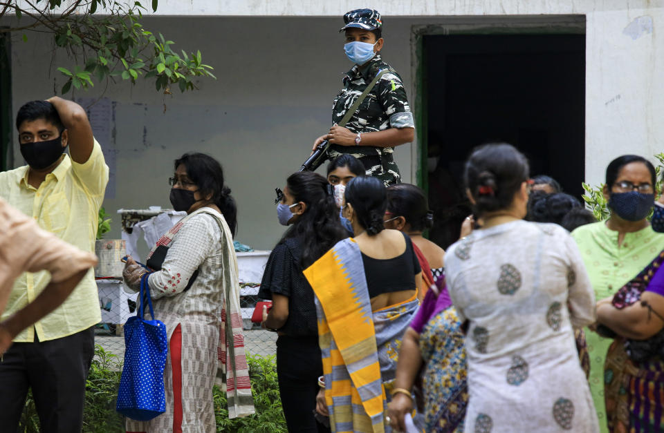 A paramilitary solder stands vigil as people stand in a queue to cast their votes outside a polling station during the fourth phase of West Bengal state elections in Kolkata, India, Saturday, April 10, 2021. (AP Photo/Bikas Das)