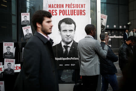 People stand next to a poster reading "Macron, President of polluters" as environmental activists block the entrance of the French bank Societe Generale headquarters during a "civil disobedience action" to urge world leaders to act against climate change, in La Defense near Paris, France, April 19, 2019. REUTERS/Benoit Tessier