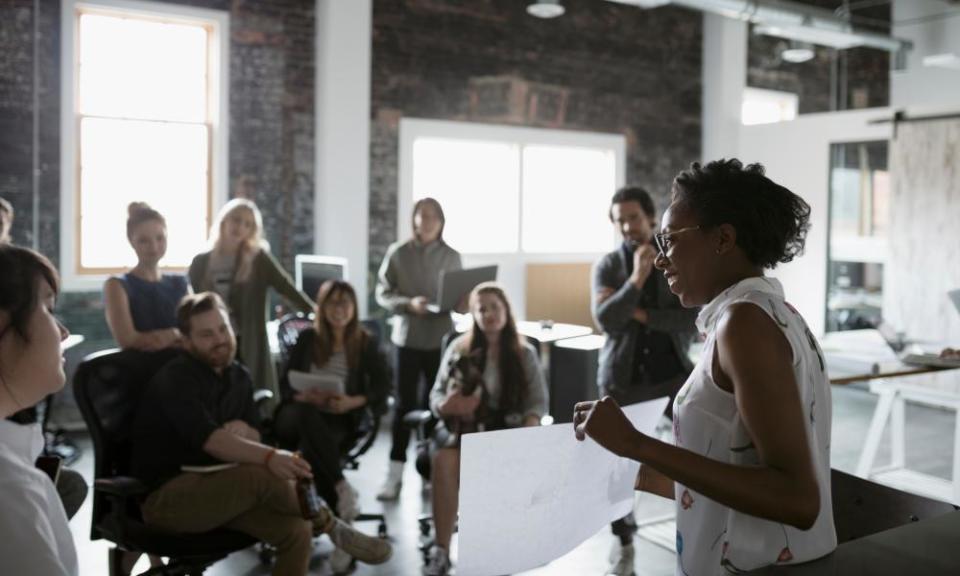 Female architect with blueprint leading meeting in open plan loft office