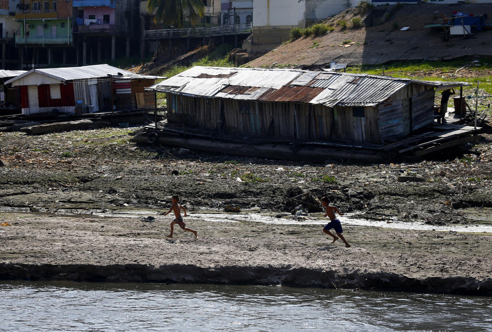 Un par de niños corren junto a una casa flotante varada en lo que solía ser la ribera del río Negro, en medio de una sequía, el martes 26 de septiembre de 2023, en Manaos, Brasil. (AP Foto/Edmar Barros)