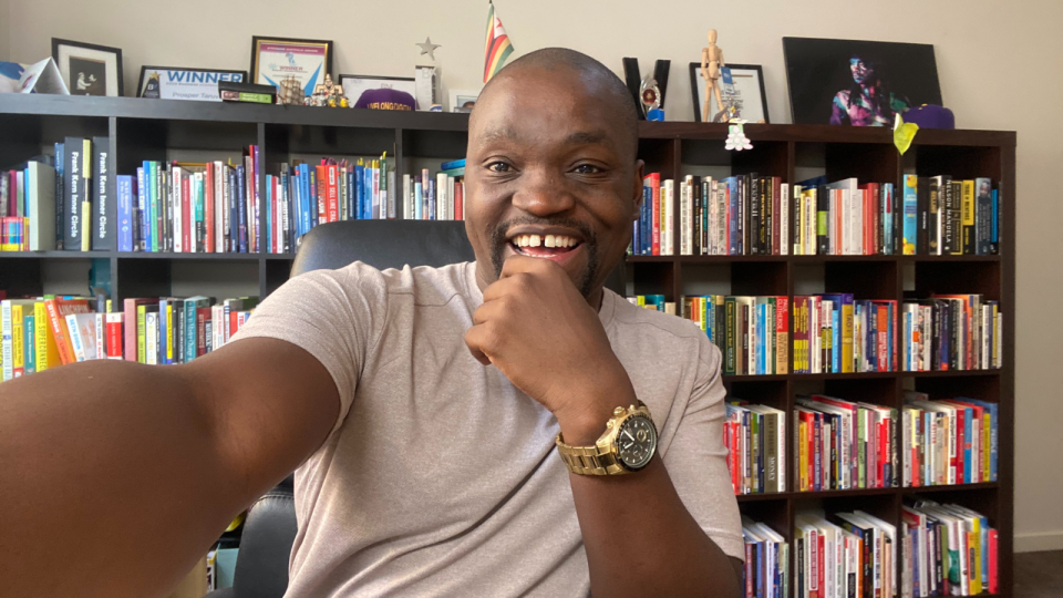 A selfie of Prosper with his book case behind him.