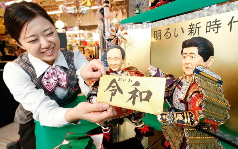 A shop worker arranges dolls depicting Mr Suga, left, and Mr Abe, holding the new era name "Reiwa" - Satoru Yonemaru/Kyodo News via AP