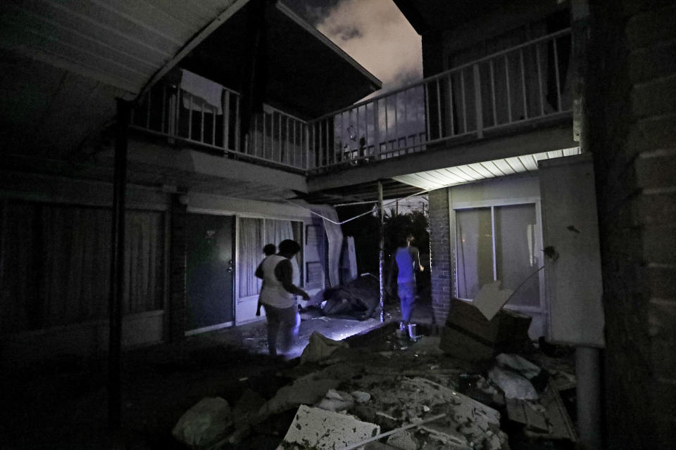 Residents walk past roofing debris at the damaged American Quality Lodge where they continue to live in the aftermath of Hurricane Michael in Panama City, Fla., Tuesday, Oct. 16, 2018. Michael's winds of as much as 155 mph (nearly 250 kph) ripped much of the roof off the two-story motel, and rain that flooded the upper level dripped down to the first floor. (AP Photo/David Goldman)