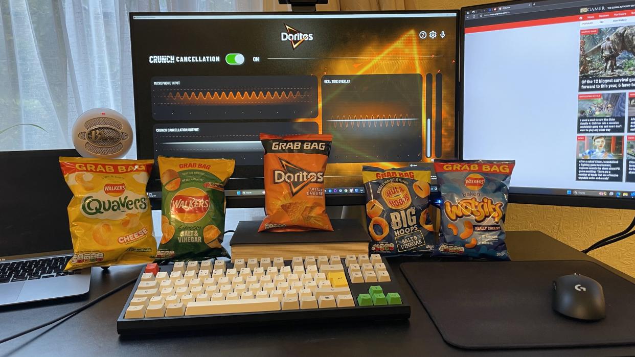  Five bags of crisps---Quavers, Walkers salt and vinegar, Doritos, Wotsits, and Hula Hoops---arrayed in a line against a computer monitor showing the Doritos Silent noise suppression software. 