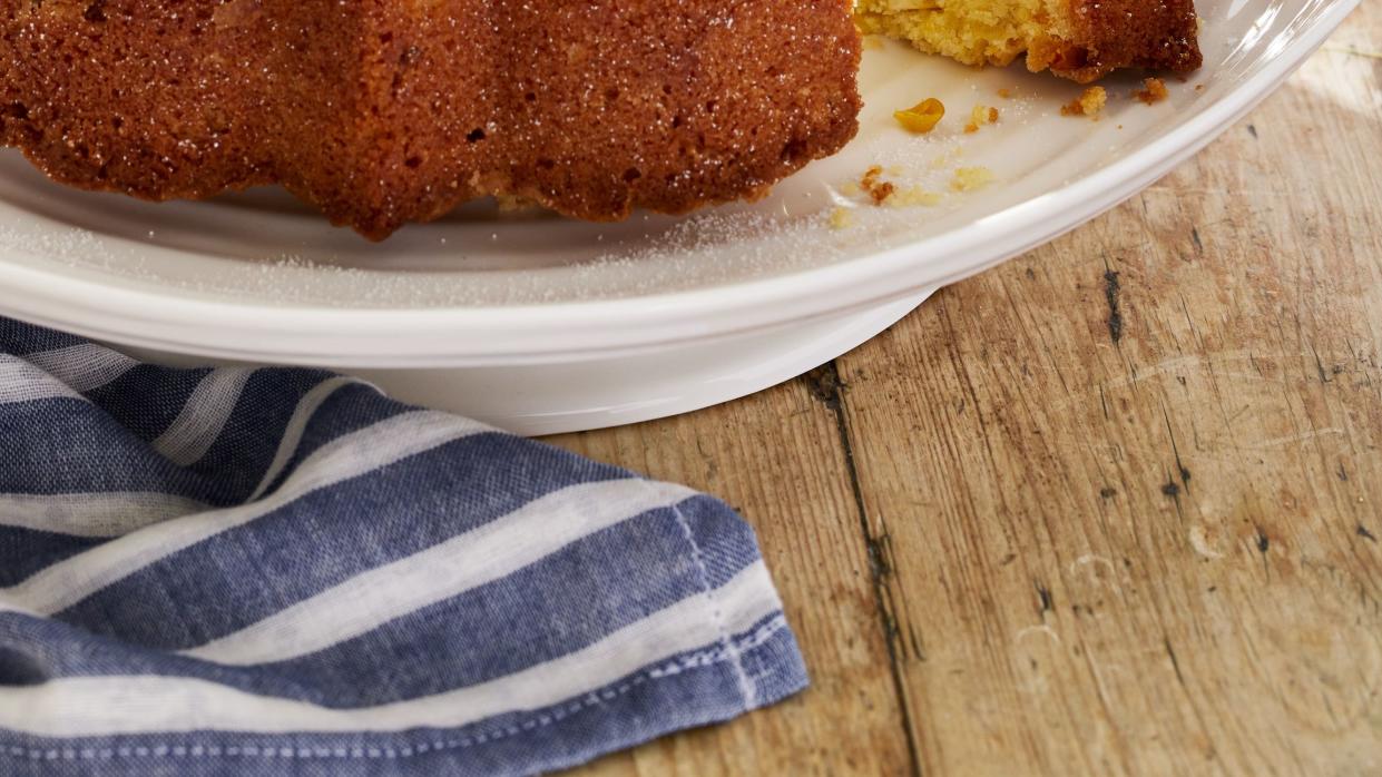 a corn bundt cake dusted with powdered sugar on a raised platter on a wooden table