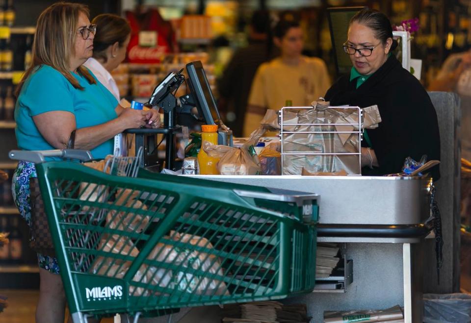 Cecilia Mas, far-left, pays for her groceries at Milam’s Market on Bird Road near Coral Gables after she waited in a long line on Friday, March 20, 2020. Mas said the store had eggs in stock, but did not have toilet paper or paper towels.