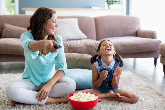 A mother and daughter watching TV and eating popcorn.