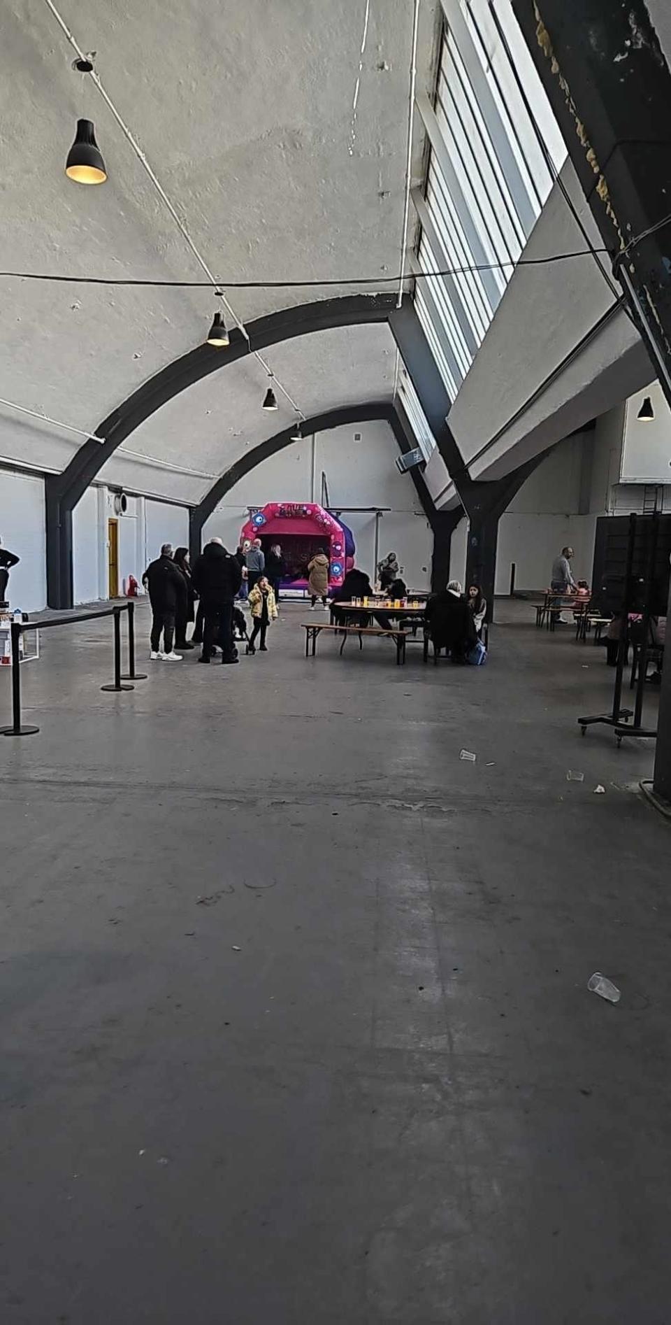 Interior of a spacious hall with arching ceilings, a few people scattered about, and a small stage setup in the distance