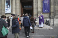 Priest Antoine d'Eudeville, right, wearing a face mask as a precaution against the coronavirus welcomes church-goers as they lineup at the entrance of the Notre-Dame-des-Champs church in Paris, Sunday, Nov. 29, 2020. French churches, mosques and synagogues can open their doors again to worshippers - but only a few of them, as France cautiously starts reopening after a second virus lockdown. Some churches may defy the 30-person limit they feel as too unreasonable, and other sites may stay closed until they can reopen for real. (AP Photo/Michel Euler)