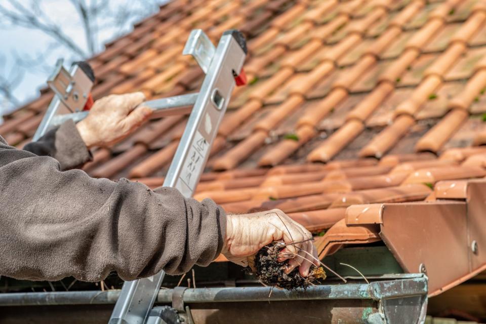 Gloved hands clean out gutters lining a red tile roof.