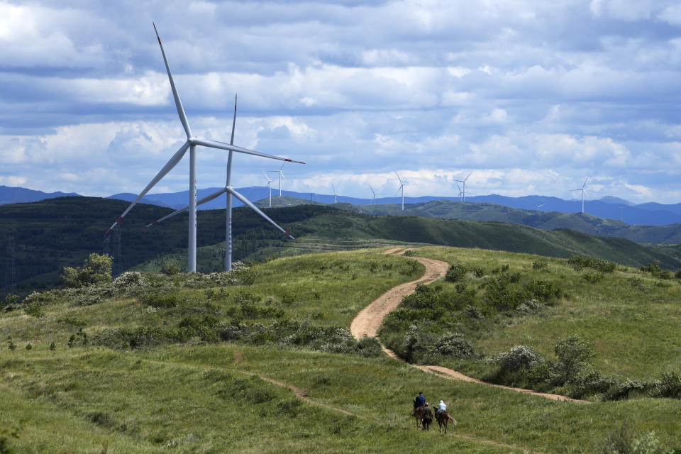 FILE - Tourists ride horses near Wind turbines on the grassland in Zhangbei county, in north China's Hebei province on Aug. 15, 2022. China, currently the top emitter of greenhouse gases in the world, aims to reach net zero by 2060, requiring significant slashing of emissions. (AP Photo/Andy Wong, File)