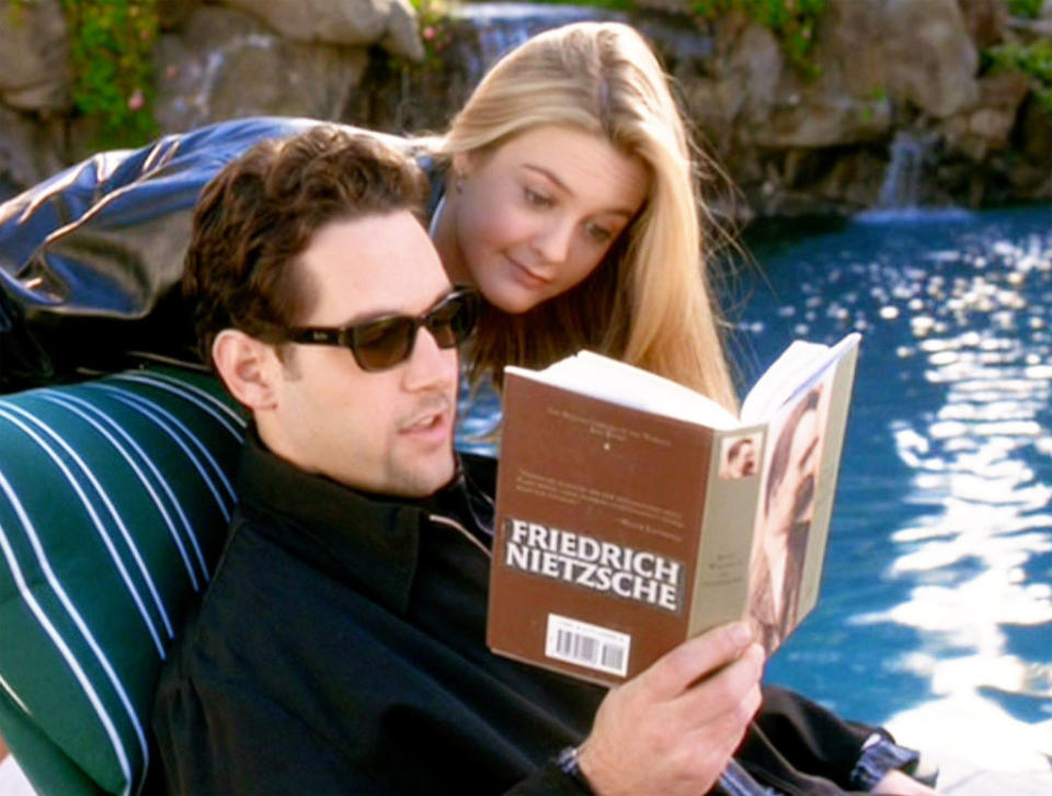 Paul's character reading a book about Friedrich Nietzsche next to a pool as Alicia's character looks over his shoulder
