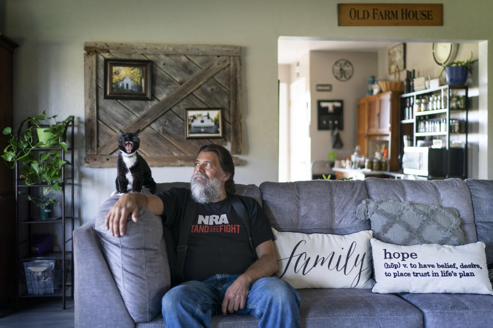 John Kraft sits next to his yawning cat, Tux, at his hilltop farmhouse in Clear Lake, Wis., Wednesday, Sept. 28, 2022. Kraft loves this place. He loves the quiet and the space but looks beyond his rural community and sees a country that many Americans wouldn't recognize. It's a dark place, dangerous, where democracy is under attack by a tyrannical government, few officials can be trusted and clans of neighbors might someday have to band together to protect one another. (AP Photo/David Goldman)