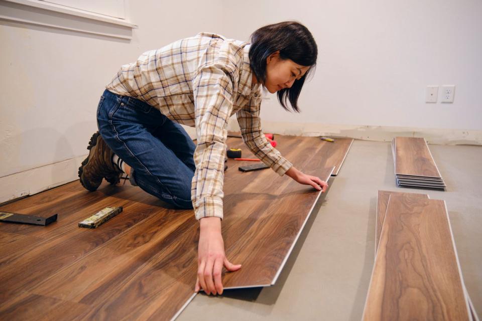 Young woman installs laminate flooring in home. 