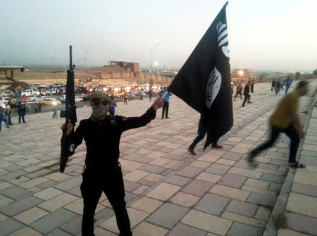 FILE PHOTO: A fighter of the Islamic State of Iraq and the Levant (ISIL) holds an ISIL flag and a weapon on a street in the city of Mosul June 23, 2014. REUTERS/Stringer/File Photo