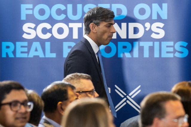 Rishi Sunak walks alongside seated people with an election poster in the background 