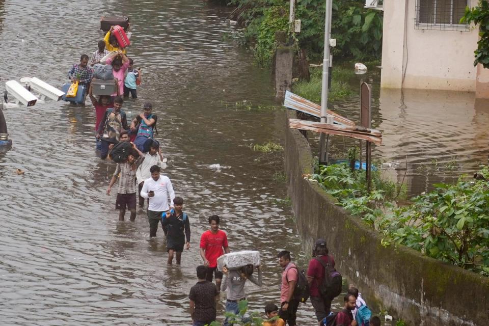 Commuters navigate a submerged street after heavy rainfall in Mumbai, India (AP)