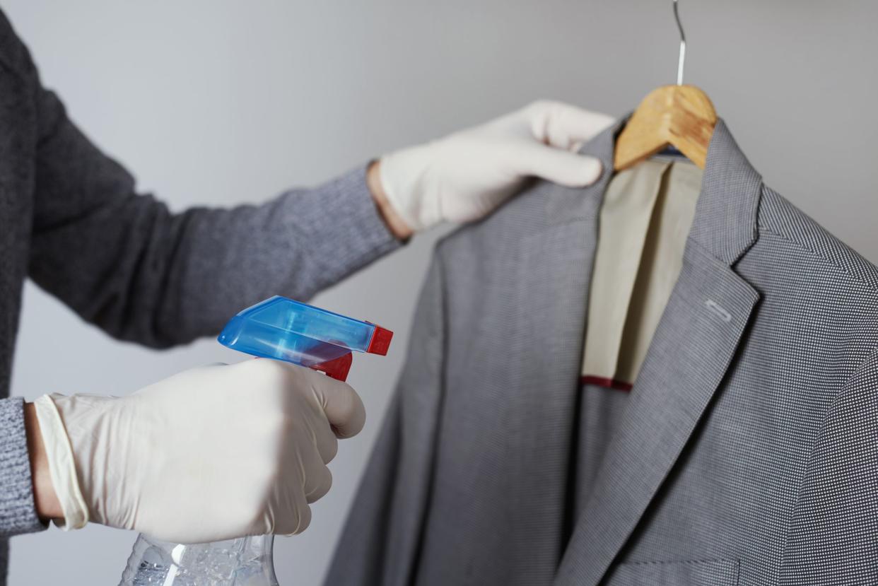 closeup of a man, wearing latex gloves, disinfecting a sport jacket hanging on a clothes hanger by spraying a disinfectant from a bottle