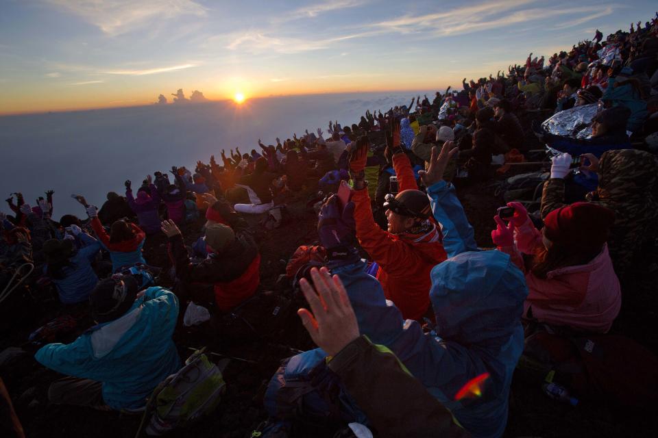 In this Sunday, Aug. 11, 2013 photo, thousands of hikers cheer from the summit of Mount Fuji in Japan as the sun rises. The Japanese cheered the recent recognition of Mount Fuji as a UNESCO World heritage site, though many worry that the status may worsen the damage to the environment from the tens of thousands who visit the peak each year. (AP Photo/David Guttenfelder)