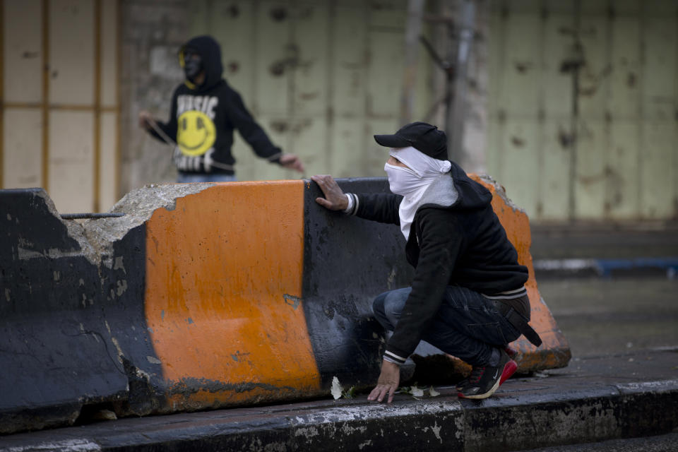 A Palestinian demonstrator take cover during clashes with Israeli troops in the West Bank city of Hebron, Monday, Dec. 9, 2019. Palestinian residents held a general strike to protest an Israeli plan to build a new Jewish neighborhood in the heart of the West Bank's largest city. (AP Photo/Majdi Mohammed)