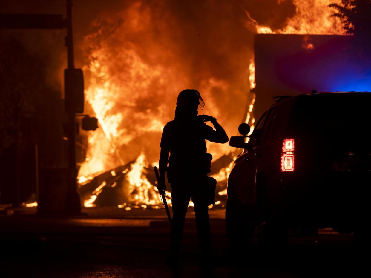 A police officer stands watch as a looted pawn shop burns behind them on 28 May, 2020 in Minneapolis, Minnesota: (2020 Getty Images)