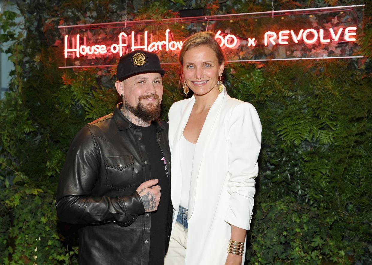 benji madden and actress cameron diaz in front of some fake grass, benji in a black leather jacket and cameron in an all white outfit with some bangles