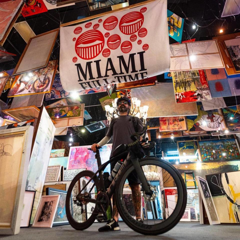 David Anasagasti, more popularly known as Ahol Sniffs Glue, strikes a pose alongside his bike and artwork for sale at Frame Art in Miami, Florida, on Friday, June 30, 2023.