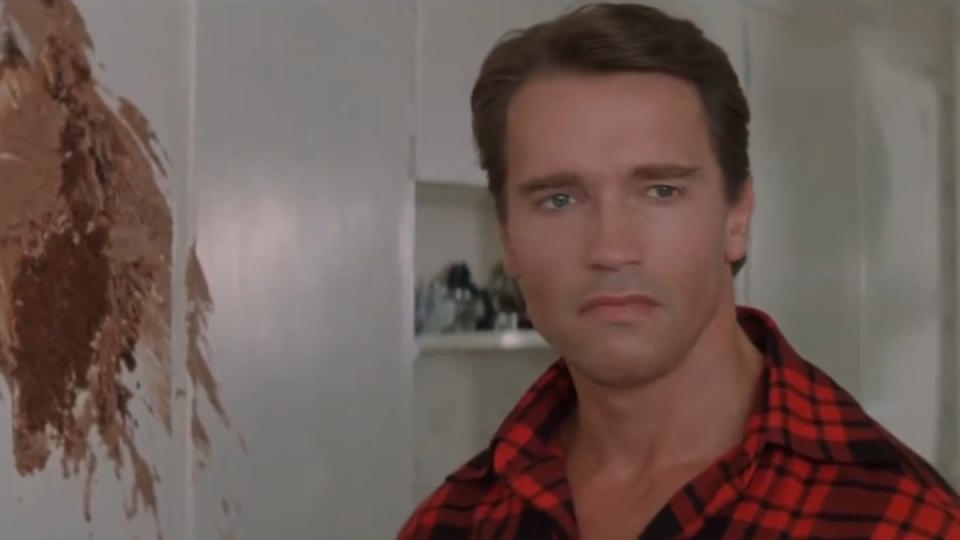 Arnold Schwarzenegger stands in a kitchen ruined by a cake in Raw Deal