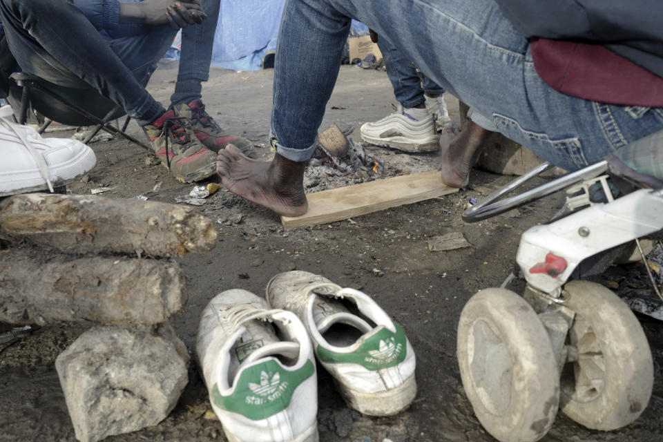 A migrant warms up his feet in a makeshift camp outside Calais, northern France, Saturday, Nov. 27, 2021. At the makeshift camps outside Calais, migrants are digging in, waiting for the chance to make a dash across the English Channel despite the news that at least 27 people died this week when their boat sank a few miles from the French coast. (AP Photo/Rafael Yaghobzadeh)