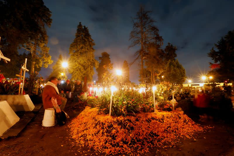 FILE PHOTO: People stand next to graves on the Day of the Dead to pay homage to their dead relatives