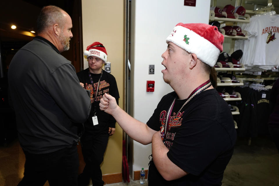 Angels for Higher representatives Matthew Adams, right, and Chase Baird, middle, greet fans at the entrance to the Arizona Coyotes' team shop prior to an NHL hockey game Dec. 3, 2021, in Glendale, Ariz. (AP Photo/Ross D. Franklin)