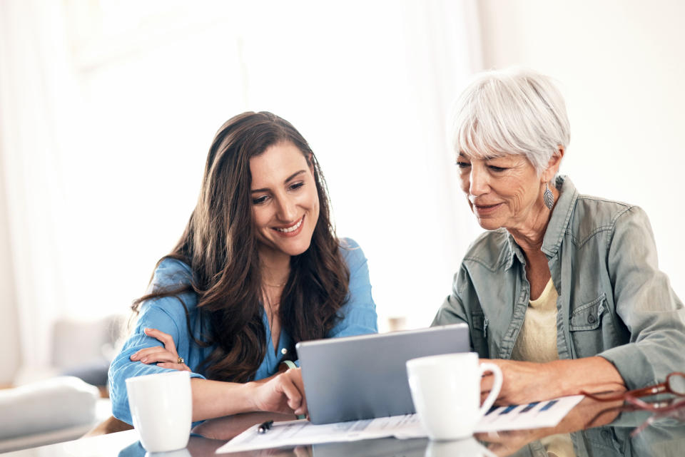 Shot of a young woman using a digital tablet with her elderly mother to help work on her home finances