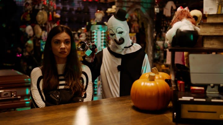 Art the Clown holds a horn in a girl's ear in a scene from Terrifier 2.