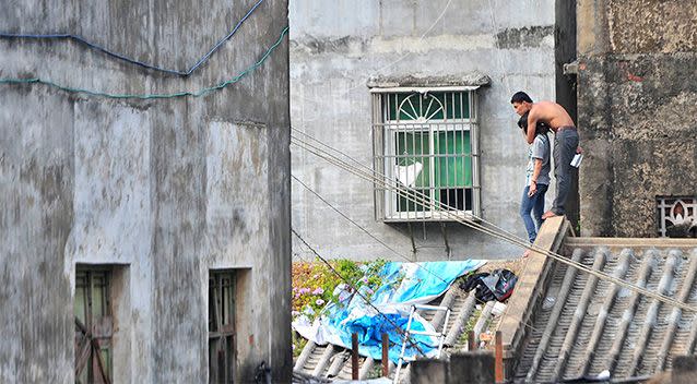 A topless man holds his girlfriend hostage with a knife atop a residential building. Photo: Reuters.