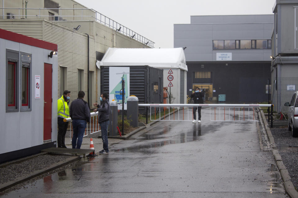 A security guard talks to people at the entrance of Novasep factory in Seneffe, Belgium, Thursday, Jan. 28, 2021. Belgian health authorities said Thursday they have inspected a pharmaceutical factory located in Belgium to find out whether the expected delays in the deliveries of AstraZeneca's coronavirus vaccines are due to production issues. The Novasep factory in the town of Seneffe is part of the European production chain for AstraZeneca's coronavirus vaccine. (AP Photo/Mark Carlson)