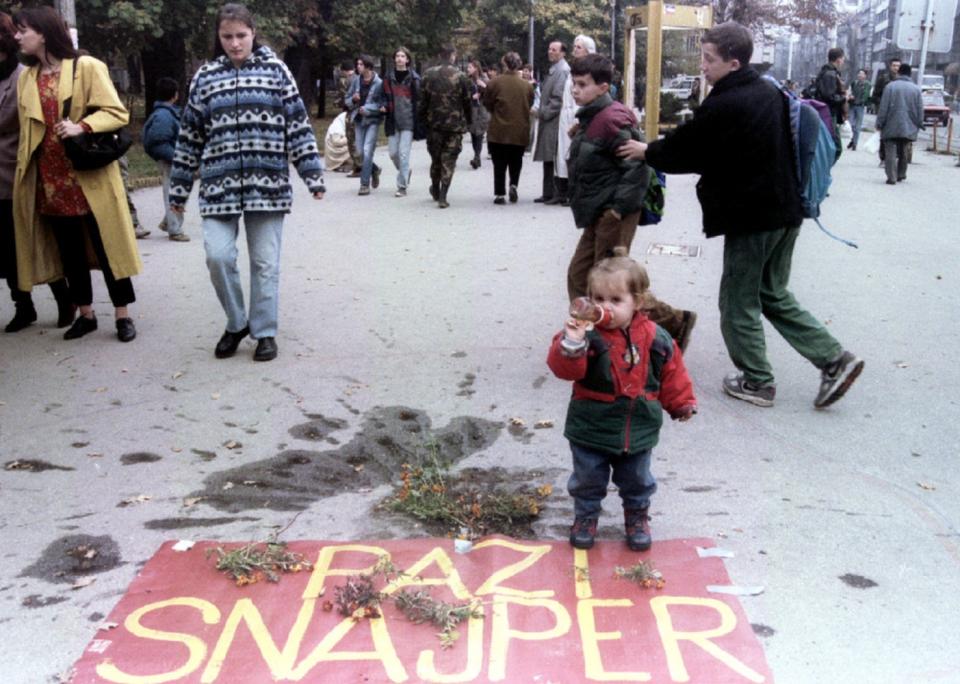 <p>Una niña permanece de pie junto a unas flores colocadas en el lugar donde una persona fue asesinada y un cartel en el que se lee ‘Cuidado con el francotirador’, en Sarajevo en noviembre de 1995. (Foto: Reuters). </p>