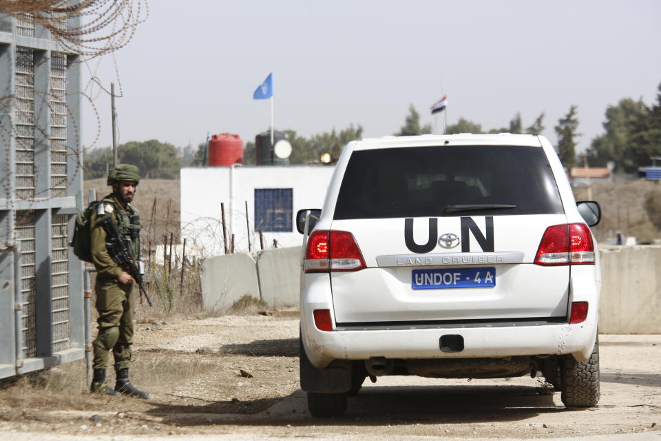 An Israeli soldier opens the border gates as an UN vehicle enters Syria in Quneitra crossing in the Israeli controlled Golan, Monday, Oct. 15, 2018. The crossing between Syria and the Israeli-occupied Golan Heights reopened for U.N. observers who had left the area four years ago because of the fighting there. (AP Photo/Ariel Schalit)