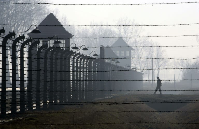 A visitor approaches a barbed wire fence and watch tower of the Auschwitz-Birkenau Nazi death camp in Poland