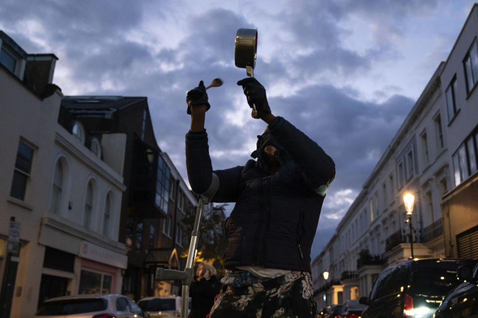 A member of the public bangs a pot outside the Chelsea and Westminster Hospital to salute local heroes during Thursday's nationwide Clap for Carers NHS initiative to applaud workers fighting the coronavirus pandemic, in London, Thursday, April 2, 2020. The new coronavirus causes mild or moderate symptoms for most people, but for some, especially older adults and people with existing health problems, it can cause more severe illness or death. (Aaron Chown/PA via AP)