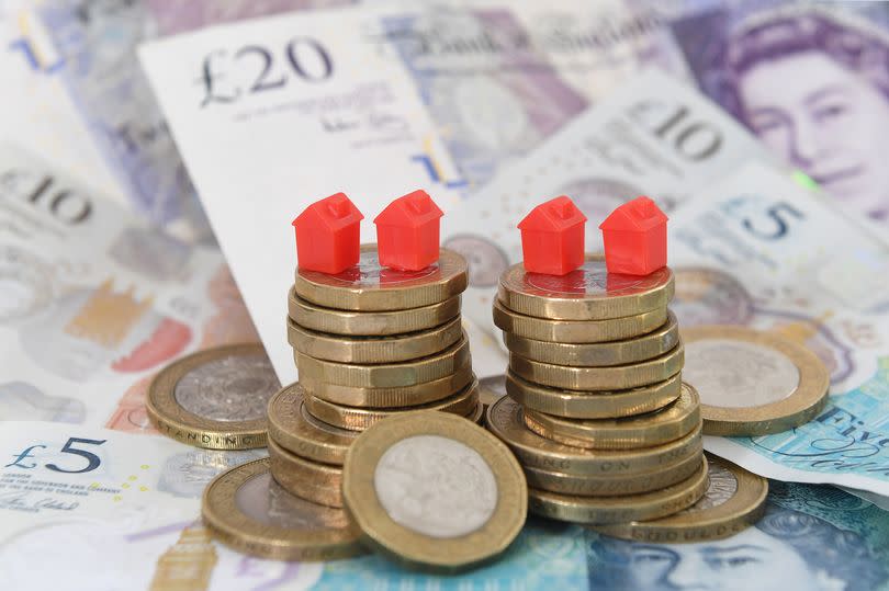 Monopoly house pieces on top of pile of £1 coins