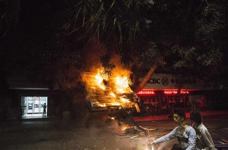 Residents ride past a burning public security kiosk during a protest against a chemical plant project, on a street in Maoming, Guangdong province, early April 1, 2014. REUTERS/Stringer