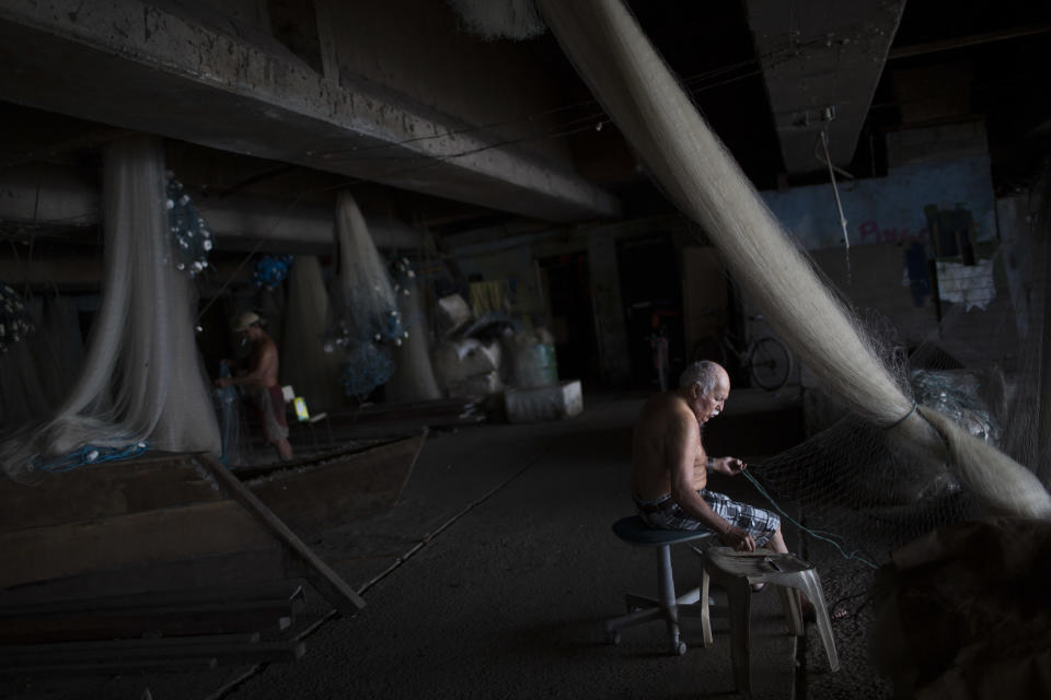 Fishermen fix their nets during a police operation to occupy the Vila Pinheiro, part of the Mare slum complex in Rio de Janeiro, Brazil, Sunday, March 30, 2014. The Mare complex of slums, home to about 130,000 people and located near the international airport, is the latest area targeted for the government's "pacification" program, which sees officers move in, push out drug gangs and set up permanent police posts. (AP Photo/Felipe Dana)