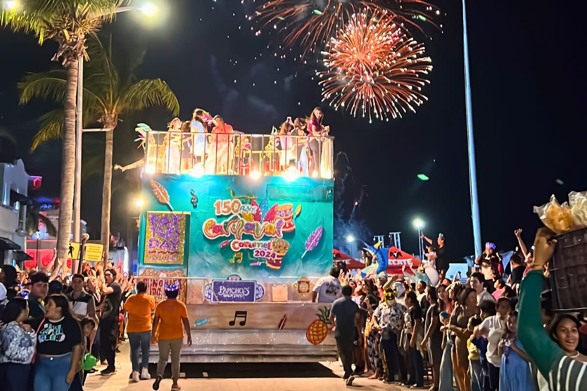 float going down the street at 2024 Cozumel Carnaval with fireworks in the sky and crowds of people