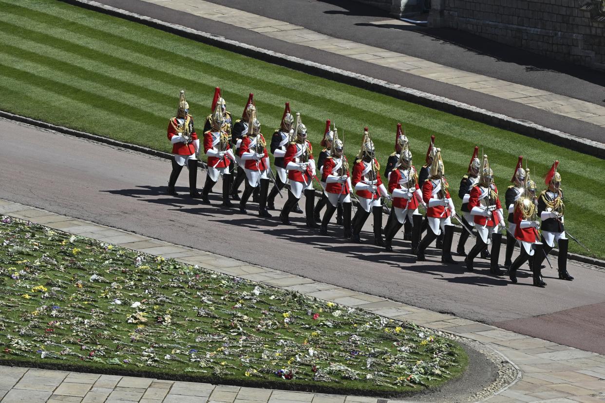 Military in parade dress uniform march past flowers which where placed on the grass for the funeral of Britain's Prince Philip inside Windsor Castle in Windsor, England, Saturday, April 17, 2021.