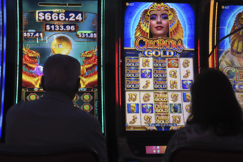 Gamblers are silhouetted against the light from slot machines on Aug. 8,2022 at the Hard Rock casino in Atlantic City N.J. Figures released on Wednesday, Feb. 15, 2023 by the American Gaming Association show the U.S. commercial casino industry won over $60 billion from gamblers in 2022, its best year ever. (AP Photo/Wayne Parry)