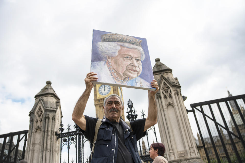 The man holds the painting over his head with the palace gates behind him