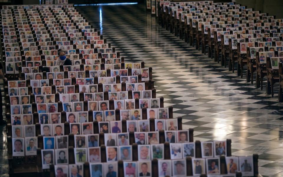 A woman sits among the more than 4 thousand portraits of people who died due to Covid-19 complications, at the Cathedral, in Lima - AP